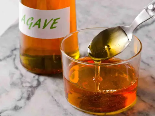 Sirope de agave en un vaso, con una cuchara vertiendo más. Ideal para endulzar recetas durante el embarazo.
