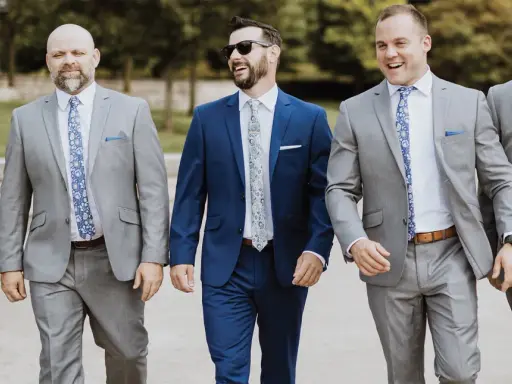 Groomsmen in grey suits and patterned ties walk together, showcasing stylish wedding pocket square folds.