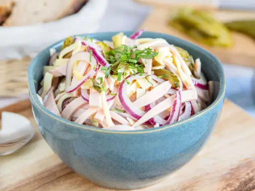 Schmackhafter schweizer wurstsalat mit roten Zwiebeln und Käse in einer blauen Schüssel, garniert mit Petersilie.