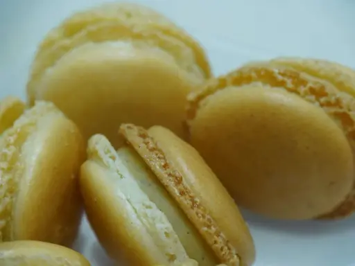 Macarons dorés à la ganache vanille, leurs coques délicates révèlent une garniture crémeuse et parfumée.