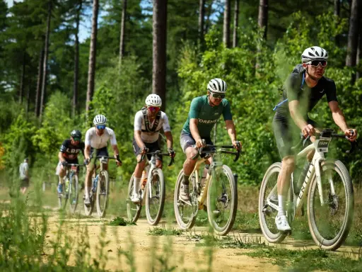 Radfahrer im Wald bei einem Gravel WM-Rennen. Staub wirbelt auf, während sie auf dem sandigen Weg fahren.