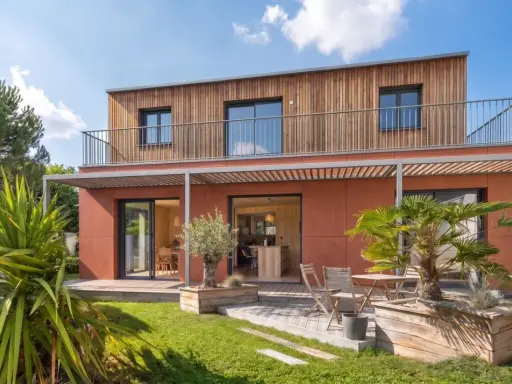 Maison moderne avec bardage bois et façade ocre. Idéal pour un conseil construction maison, avec jardin verdoyant et terrasse accueillante.