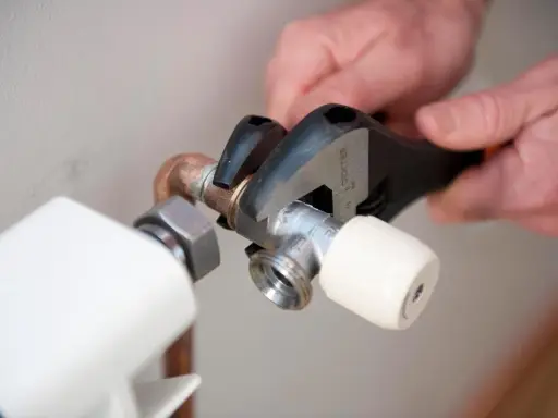 Manos ajustando llave de radiador con llave inglesa para cambiarla y evitar goteos.