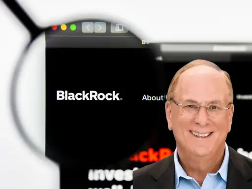 Uśmiechnięty mężczyzna w okularach, obok logo BlackRock. Larry Fink, jeden z założycieli BlackRock, na tle strony internetowej firmy.
