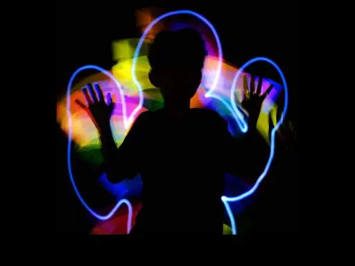 Silueta de niño jugando con light painting, creando auras de colores vibrantes a su alrededor.