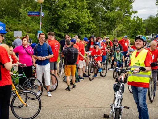 Uczestnicy rajdu rowerowego w czerwonych koszulkach, dzieci i dorośli, gotowi do startu.