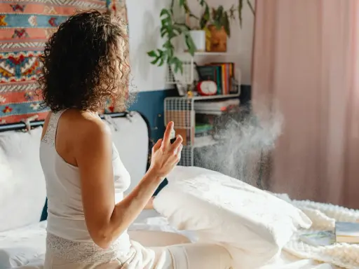 Mujer rocía almohada con spray para eliminar el olor fétido en una habitación.