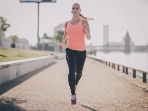 Frau joggt am Fluss entlang. Sie beweist, dass ist joggen gesund und ein toller Start in den Tag.