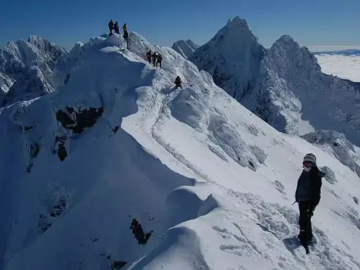 Zimowy trekking po graniach Tatr, gdzie śnieg tworzy prawdziwą koronę gór polskich. W oddali widać morze chmur.