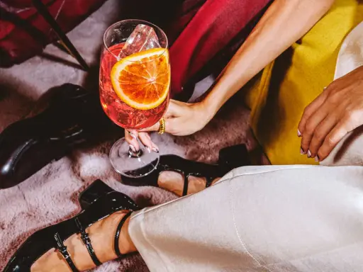 Elegancka kobieta z drinkiem, w którym widać plaster pomarańczy i lód. Zastanawiasz się, wermut co to? To aromatyzowane wino, idealne na letnie wieczory.