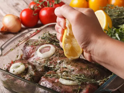 Fleisch marinieren für den Grill: Zitrone über mariniertes Fleisch mit Zwiebeln und Kräutern ausdrücken.