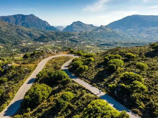 Ein Rennradfahrer auf Kreta genießt die kurvenreiche Straße durch eine grüne Berglandschaft.