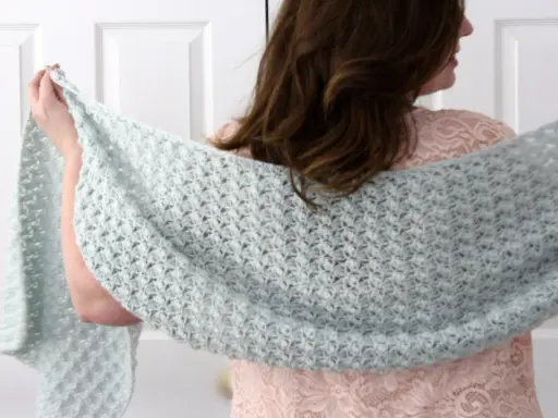 Mujer con chal rectangular de crochet azul claro sobre vestido rosa.