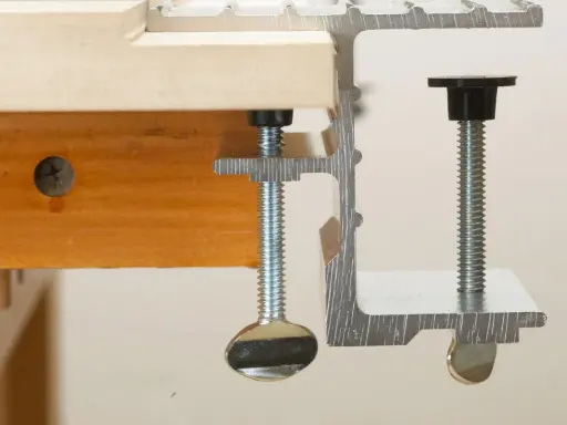 Dos tipos de abrazaderas metálicas sujetan una tabla de madera.