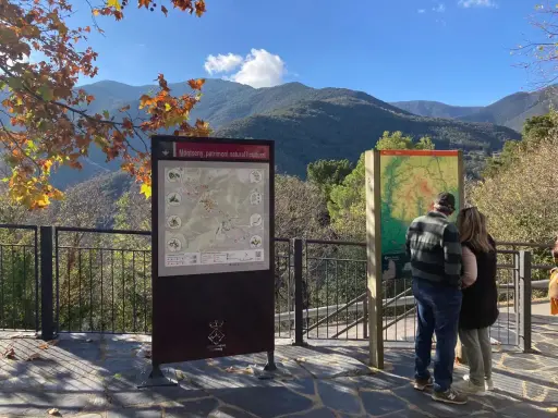 Pareja observa mapa de senderismo en los valles oriental de Montseny. El paisaje montañoso y el follaje otoñal crean un entorno pintoresco.