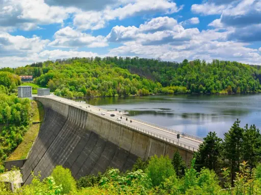 Die Talsperre im Harz staut einen See, umgeben von grünen Wäldern unter einem blauen Himmel mit weißen Wolken.