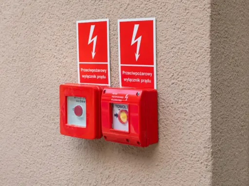 Dwa czerwone przyciski awaryjne z tabliczkami "Przeciwpożarowy wyłącznik prądu". Przepisy bezpieczeństwa wymagają ich stosowania.