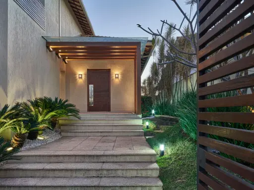 Un portico moderno con porta in legno scuro, illuminazione soffusa e piante rigogliose. Un esempio di come abbellire un portico con stile e natura.