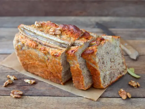 Pyszny chlebek bananowy z bakaliami, pokrojony w kromki, z widocznymi orzechami i bananem na wierzchu.