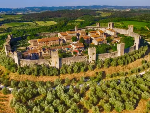 Borgo medievale fortificato su una collina, circondato da uliveti e vigneti. Bellissimi paesaggi toscani sotto un cielo azzurro.