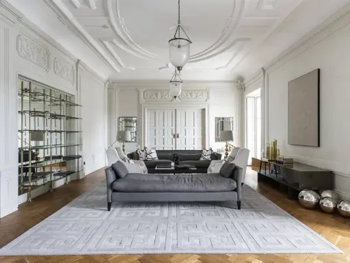 Ett elegant vardagsrum med detaljerad stuckatur och dubbeldörrar. Malin Glemme skulle älska den lyxiga inredningen med soffor, bokhylla och konst.