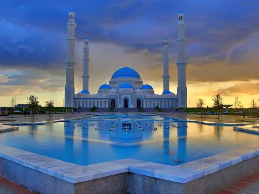 Die Hazrat-Sultan-Moschee in Astana, ein architektonisches Meisterwerk, spiegelt sich im Wasser eines Brunnens unter einem dramatischen Abendhimmel.