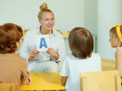 Nauczycielka pokazuje literę "A" grupie dzieci. Jedno z dzieci, 6-latek, uważnie słucha.