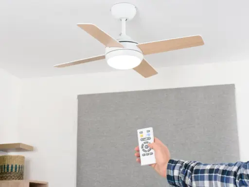Mano con mando a distancia operando un ventilador de techo escayola con luz integrada.
