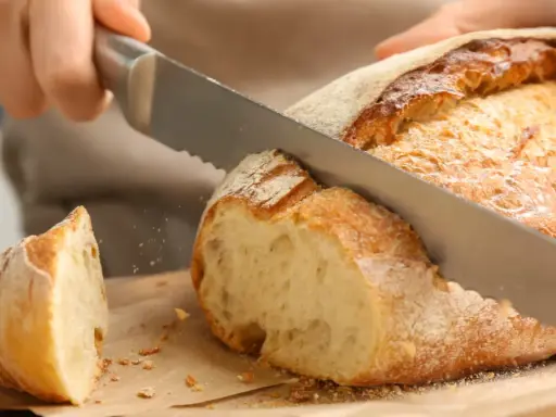 Krojenie świeżo upieczonego bochenka, idealnego na domowy przepis na chleb pieczony w piekarniku. Chrupiąca skórka i miękki środek.
