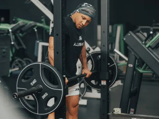 Mann im Fitnessstudio bereitet sich auf schwere myo reps vor, hält eine Langhantel mit 20kg Scheiben.