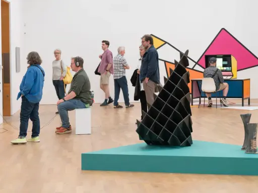 Visitors explore diverse artworks in what is an art gallery, from video installations to abstract sculptures and colorful wall art.
