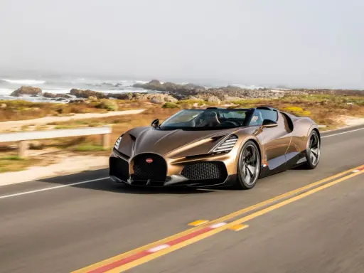 Ein bronzener Bugatti Mistral fährt auf einer Küstenstraße.