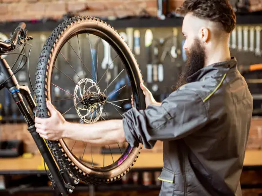 Mechanik z brodą sprawdza oponę gravelową roweru. Zastanawia się, ile mleka do opony gravel będzie potrzebne, by zapewnić najlepszą przyczepność.