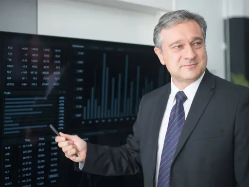 Mężczyzna w garniturze wskazuje na ekran z danymi finansowymi, wyjaśniając, kto płaci doradcy kredytowemu.