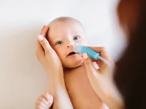 Mama delikatnie oczyszcza nosek niemowlaka z katarem za pomocą aspiratora.