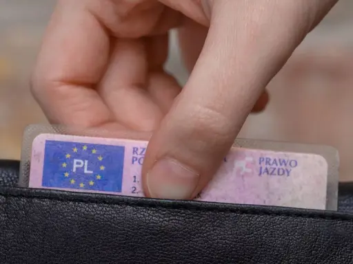 Dłoń wyjmuje z czarnego portfela polskie prawo jazdy.