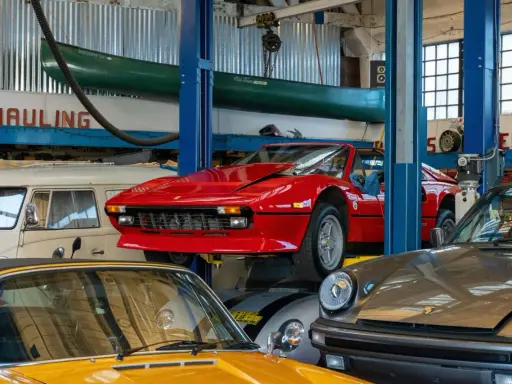 Taller mecánico con autos clásicos: un rojo Ferrari en elevador, un Porsche gris y un amarillo. ¡Ideas para tu taller!