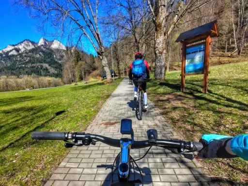 Rowerzyści przemierzają malowniczą ścieżkę rowerową w Szczawnicy, podziwiając górskie krajobrazy.