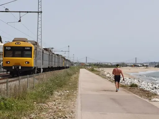 Gelber Zug fährt entlang der Küste von Cascais nach Lissabon. Ein Mann joggt am Strand entlang.