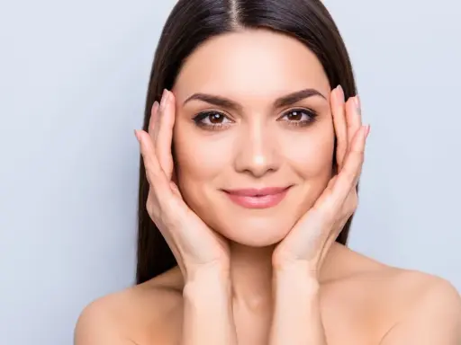 Mujer con piel radiante, resultado del colágeno para la piel. Sus manos acarician su rostro, mostrando una tez suave y luminosa.