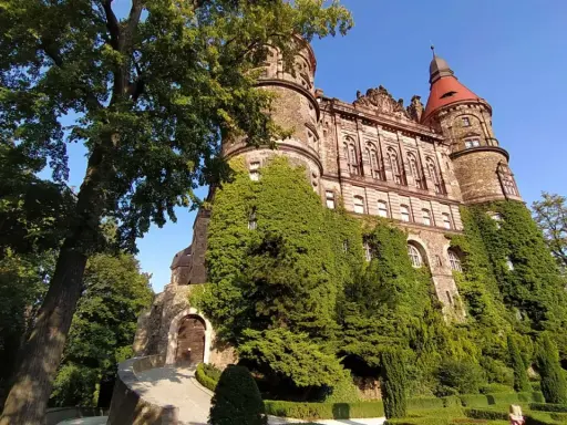 Imponujący zamek porośnięty bluszczem, z czerwoną wieżą i zadbanym ogrodem. Sprawdź zamek książ cennik przed wizytą.