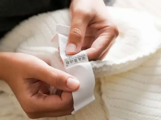 Dłonie trzymają białą metkę z symbolami pielęgnacji. To oryginalna metka Off-White, która informuje o sposobie prania swetra.