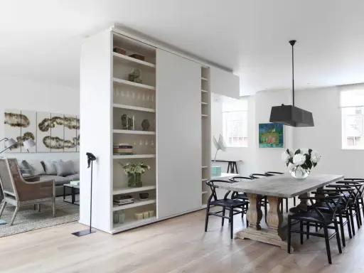 En vit rumsavdelare etta med hyllor delar av ett modernt vardagsrum och matplats.