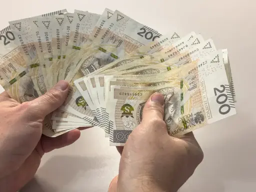 Dłonie trzymają wachlarz banknotów 200 zł. Zastanawiasz się, ile to brutto, jeśli 4200 netto to Twoja pensja?