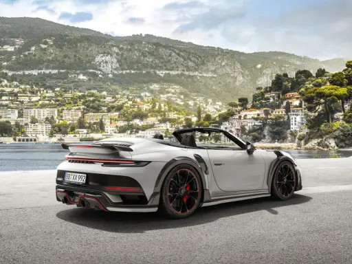 Ein weißer Techart GTstreet RS Cabriolet steht an einer Küstenstraße mit Blick auf eine malerische Stadt am Hang.
