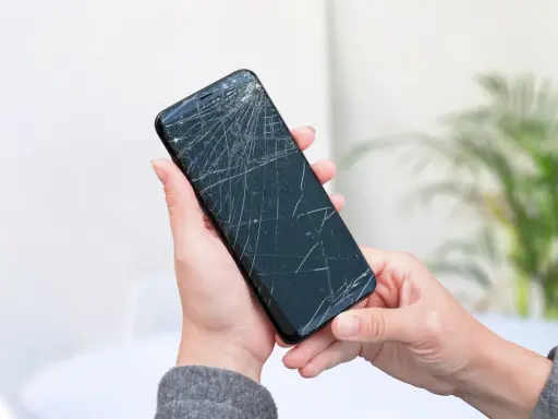 Dłoń trzyma pęknięty telefon, czekając na wymianę ekranu.