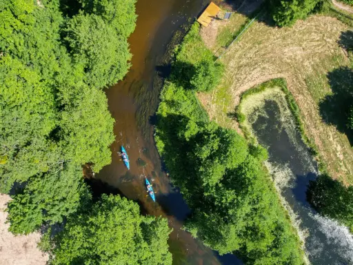 Dwie kajaki płynące rzeką wśród zieleni. To wspaniałe **kociewie atrakcje** dla miłośników przyrody i aktywnego wypoczynku.