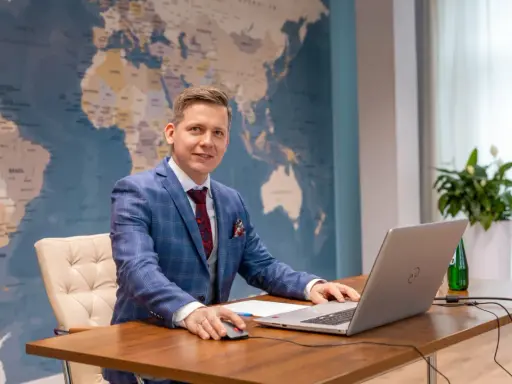 Mężczyzna w garniturze przy biurku z laptopem, na tle mapy świata. Tak wyglądają studia doktoranckie w dzisiejszych czasach – globalne spojrzenie i praca z technologią.