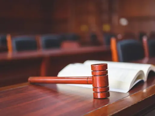 Młotek sędziowski i otwarta księga na drewnianym stole. Może to symbolizować formalne zrzeczenie się swojej części mieszkania w sądzie.