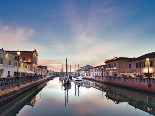 Canale di Cesenatico al tramonto, con barche a vela ormeggiate e riflessi sull'acqua. La riviera cesenatico incanta con i suoi colori.